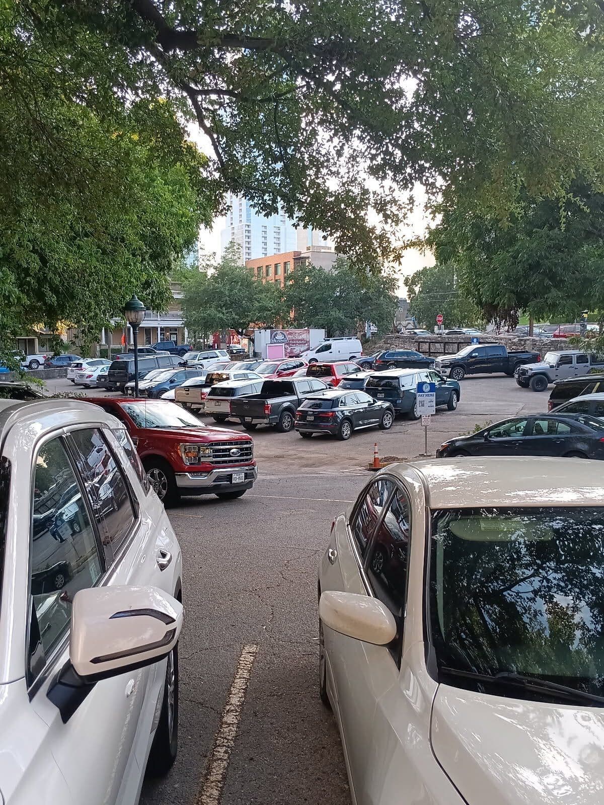 The ANW lot packed full of cars on a weekday morning, downtown Austin's skyline through the trees