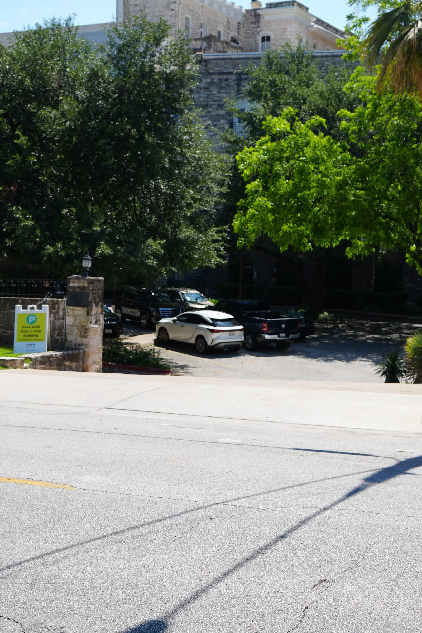 A row of cars parked along the perimeter of the ANW lot, framed by mature trees