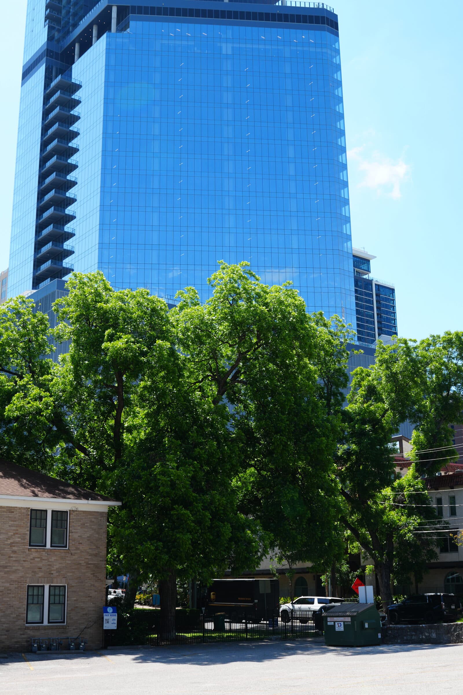 A downtown Austin glass tower rising above the trees beside the ANW lot